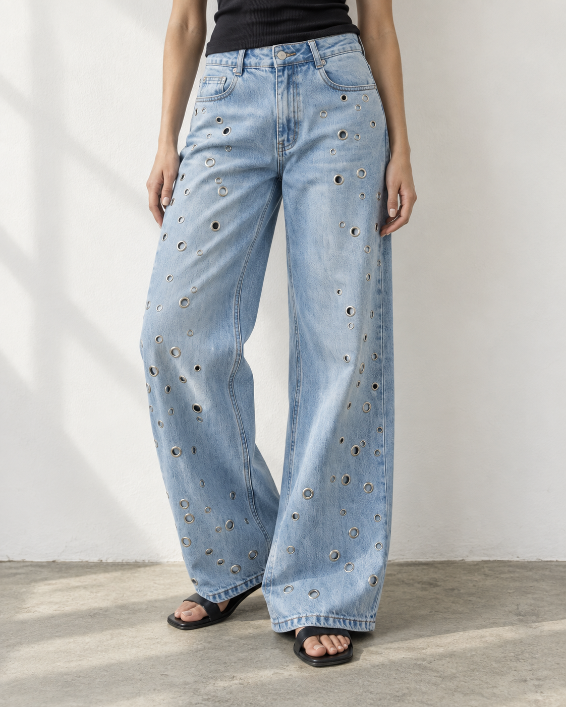 Detalhe do jeans wide leg azul-claro com ilhoses, da cintura aos pés.